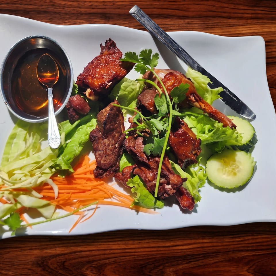 Crispy duck pieces with fresh lettuce, shredded carrots, cucumber slices, and a side of sauce.