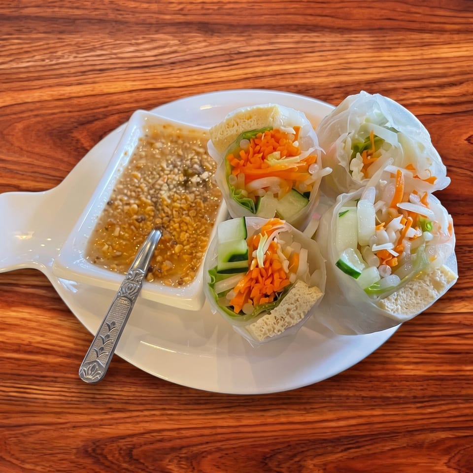 Four fresh spring rolls with vegetables and tofu, served with peanut sauce on a white plate.