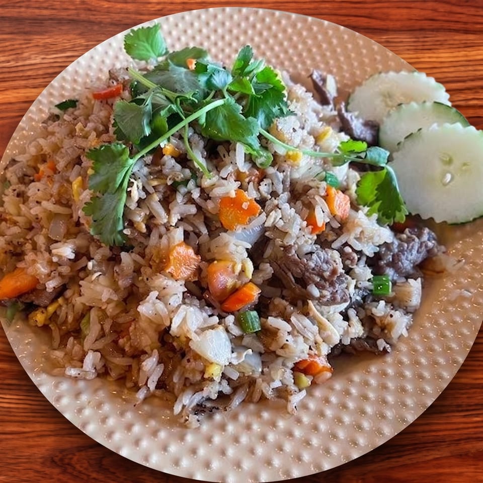 Fried rice with beef, carrots, and cilantro, served with cucumber slices on a textured plate.