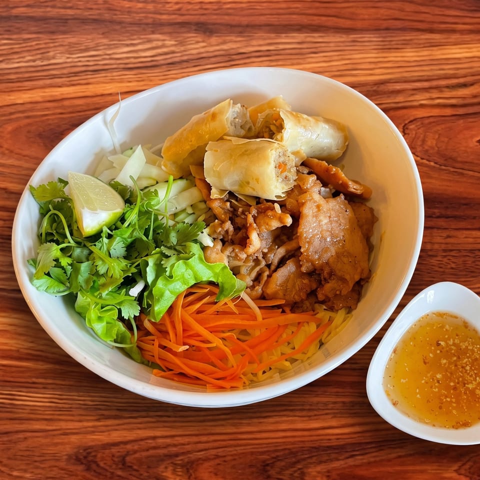Vietnamese vermicelli bowl with grilled pork, crispy spring rolls, fresh herbs, and a side of fish sauce.